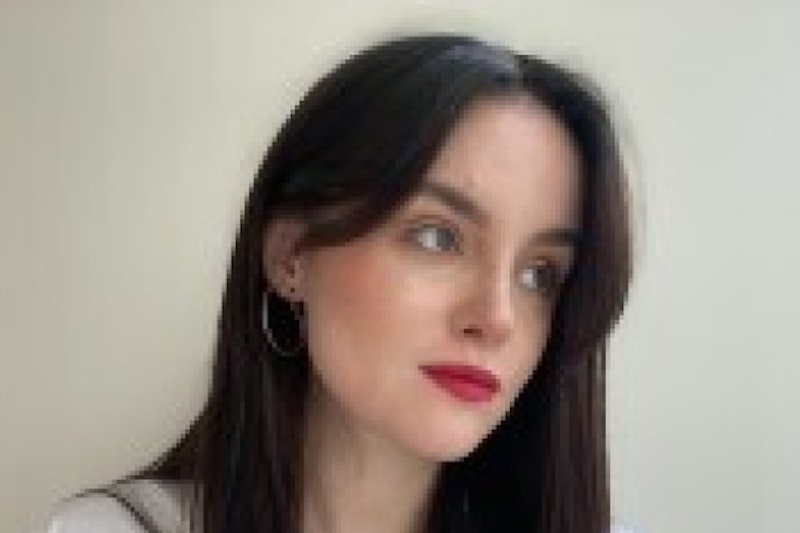 Picture of Iris who is a young women with brown hair. She is wearing a white top & red lipstick. She is looking to the right.